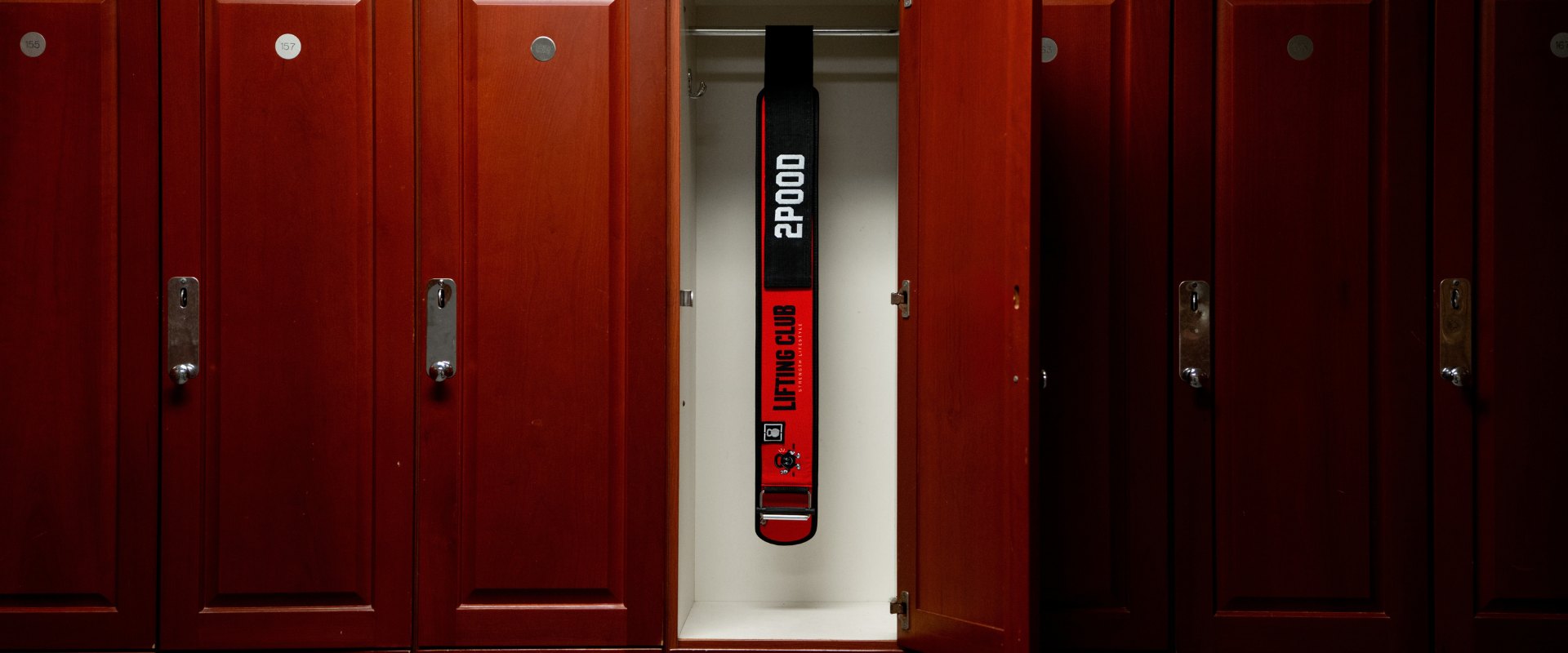 A 2POOD Lifting Club weightlifting belt hanging in an open gym locker.